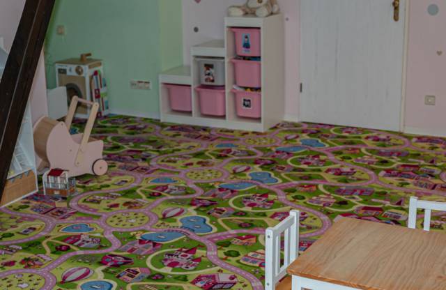 Puppenstube mit buntem Straßenteppich, Tisch, Puppenwagen und Spielbereich im Eck