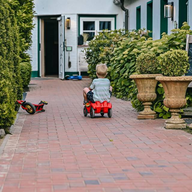 Kleiner Junge fährt mit Bobbycar am Hotel entlang
