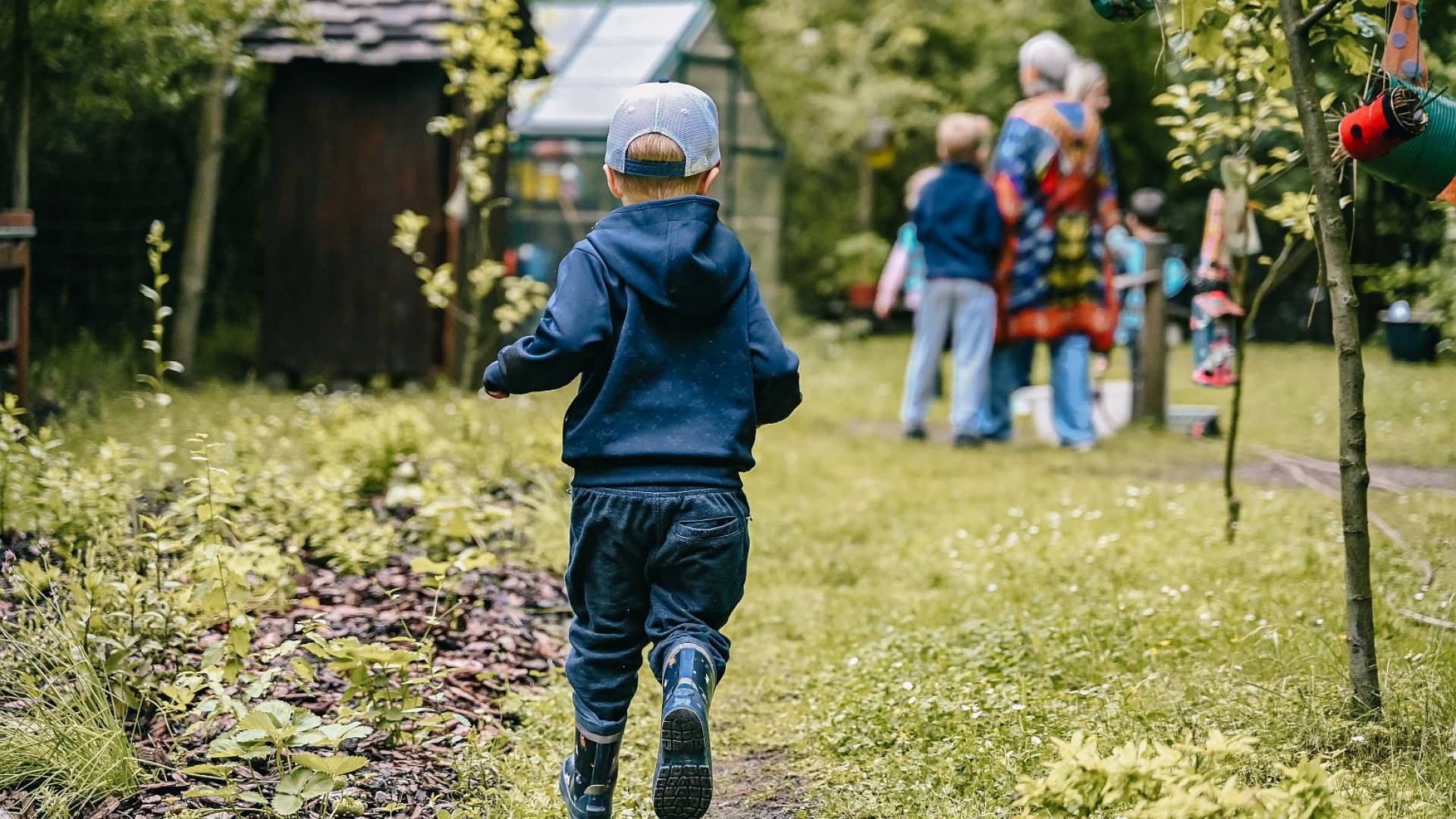 kleiner Junge läuft im Garten mit Gummistiefeln zu Familie