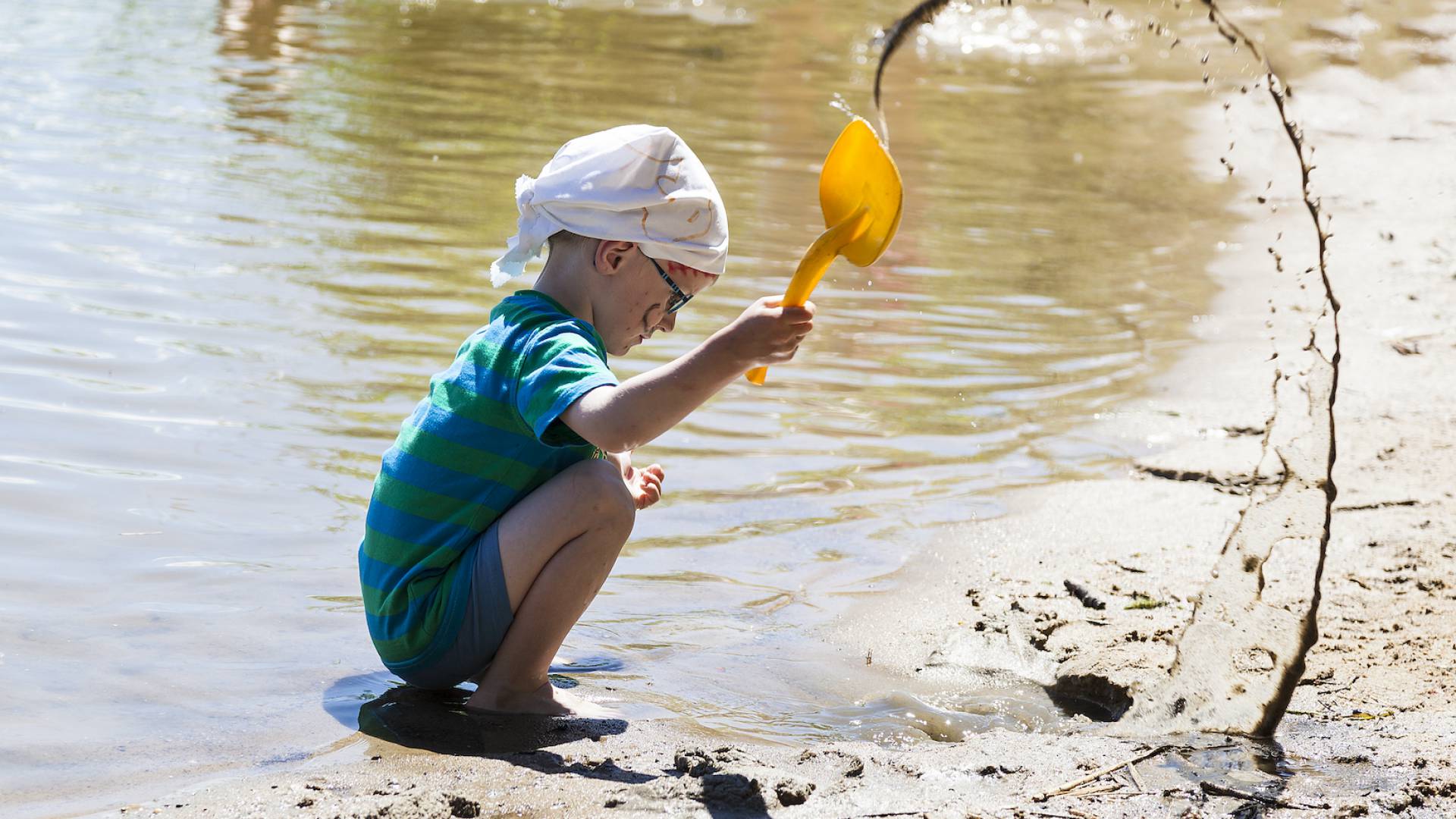 Junge spielt mit Sand am Wasser