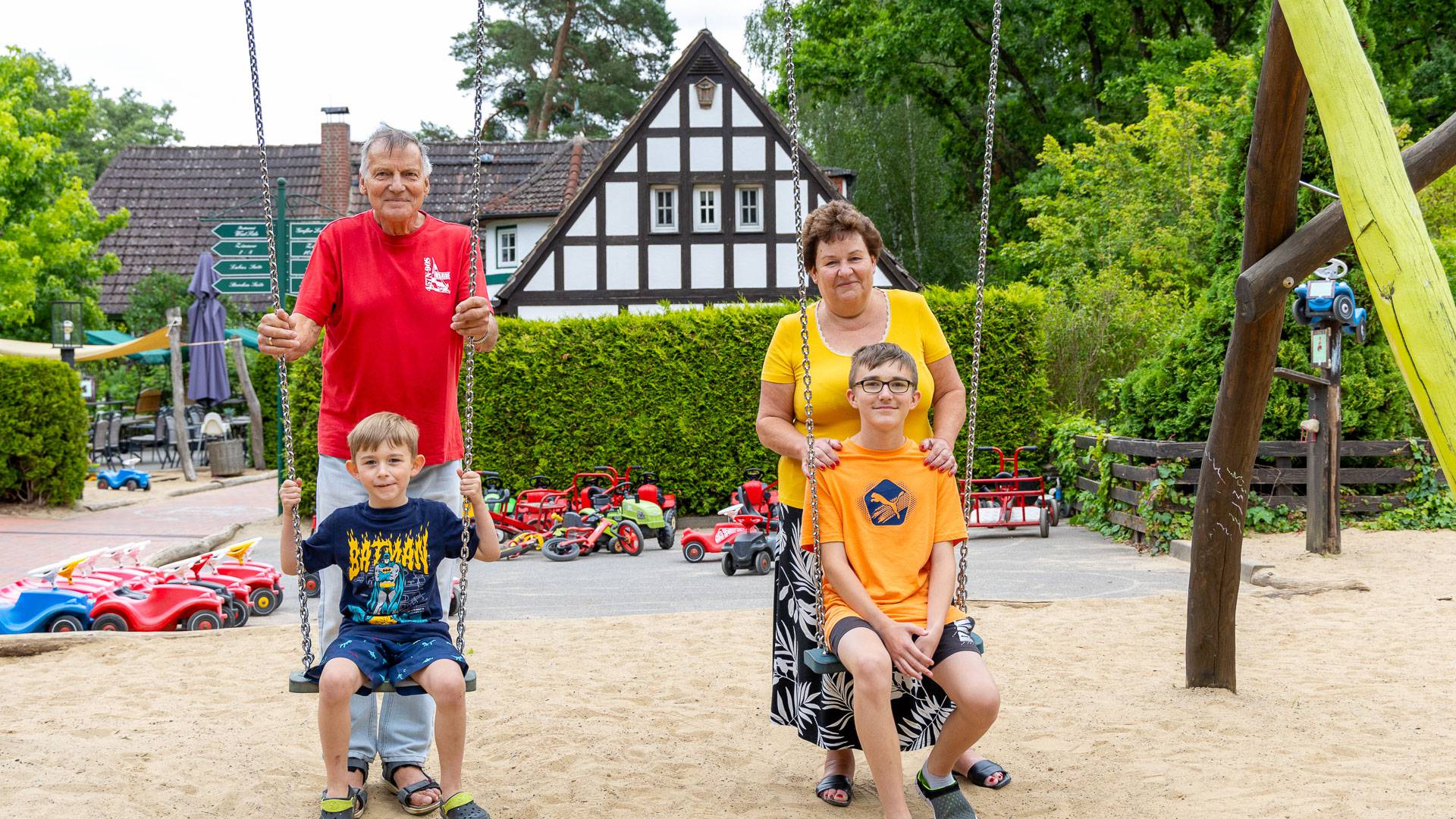 Kinder auf einer Schaukel mit Oma und Opa auf dem Spielplatz des Familienhotels