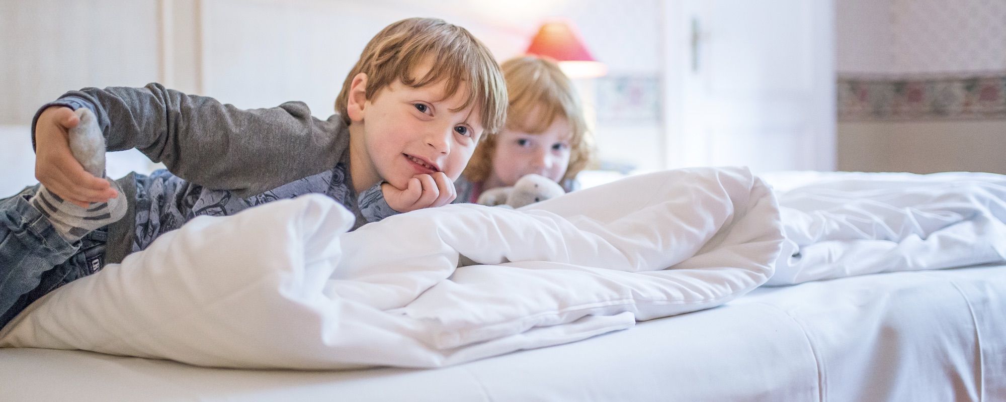 Familienhotel Borchard`s Rookhus an der Mecklenburgischen Seenplatte: Zwei Kinder liegen auf einem gemütlichen Bett im Familienzimmer